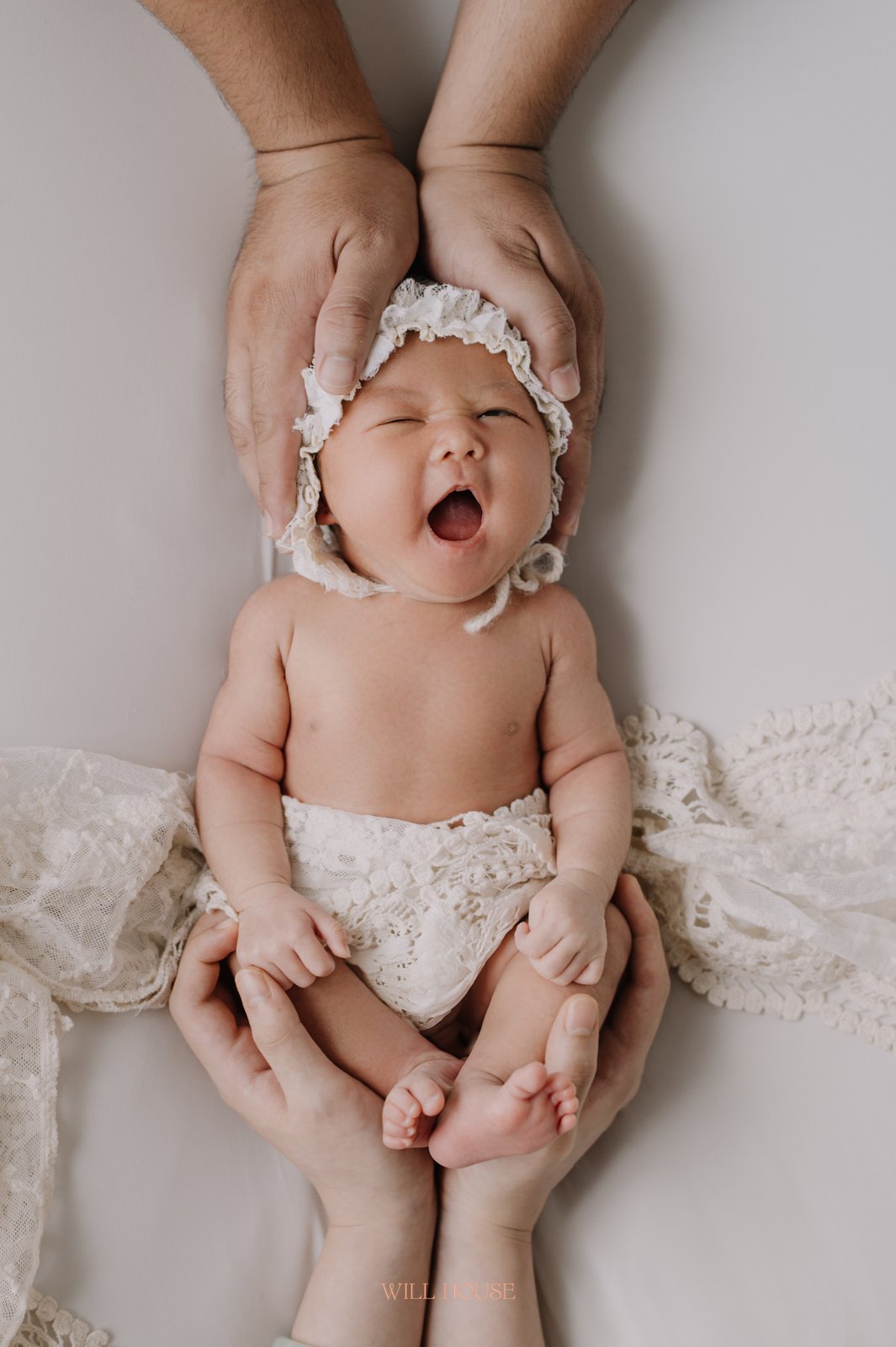 Ba mẹ nâng niu bé sơ sinh đội mũ ren, bé mở miệng ngáp