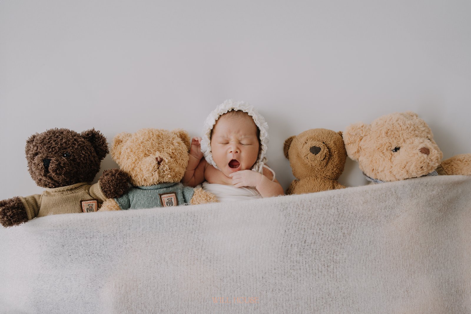 Bé sơ sinh đội mũ len nằm cùng dãy thú bông