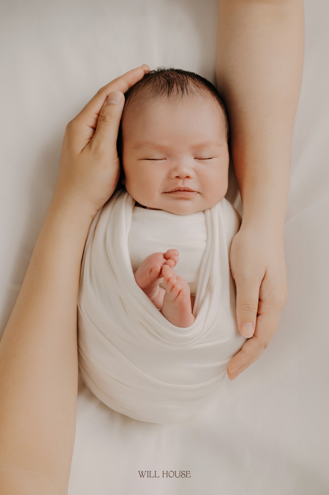 Ảnh newborn tại Will House Studio Cần Thơ, bé được ba mẹ nâng niu bên khăn quấn trắng